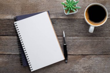 Yukarıdan bakıldığında boş bir defter ve ahşap masa arkasında kahve görünüyor. Tasarımcının evde yaratıcı çalışması için bir iş yeri. Fotokopi alanı olan düz alan, işletme finansmanı veya eğitim kavramı.