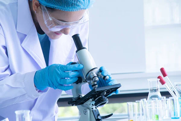 Asian woman scientist, researcher, technician, or student conducted research or experiment by using microscope which is scientific equipment in medical, chemistry or  biology laboratory — Stock Photo, Image