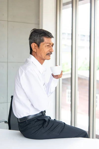 Asian Business old man with white shirt working with labtop thinking, planning and drinking coffee in the meeting room at the modern office. Businessman order team in the office