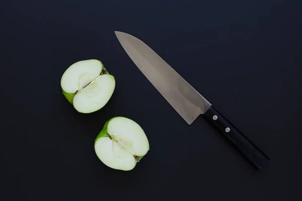 Deux moitiés de pomme verte et couteau sur fond noir — Photo