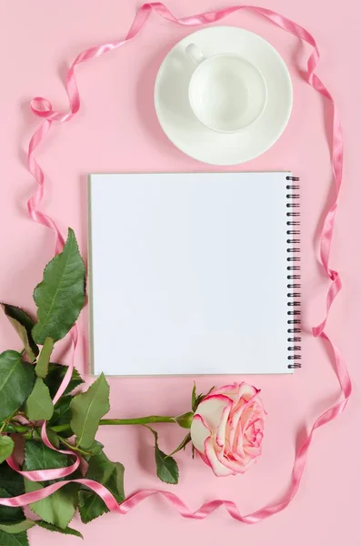Virágzó friss rózsaszín rózsa virág, csésze kávé és notebook rózsaszín háttér — Stock Fotó