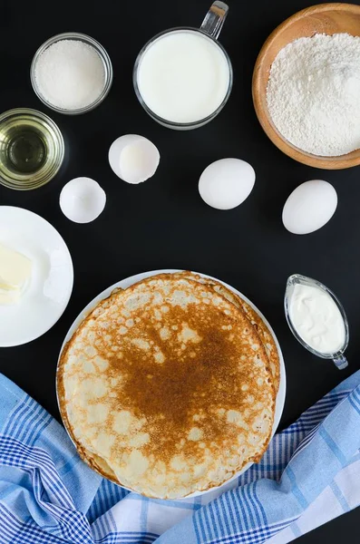 Russian pancakes with ingredients for cooking on black background — Stock Photo, Image