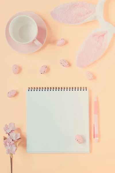 Easter holiday background with notebook and pen, cup for coffee, bunny ears and easter eggs