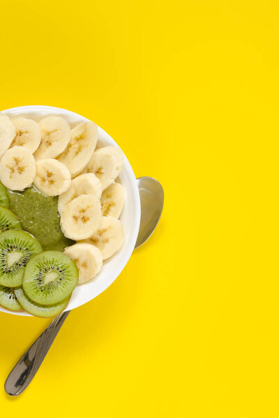 Green smoothie in a white bowl on yellow background