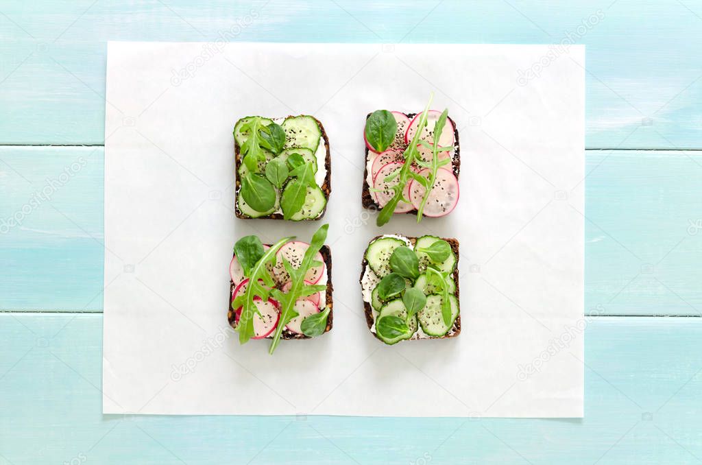 Sandwiches with cream cheese, fresh cucumber, radish, chia seeds and arugula on mint wooden background.