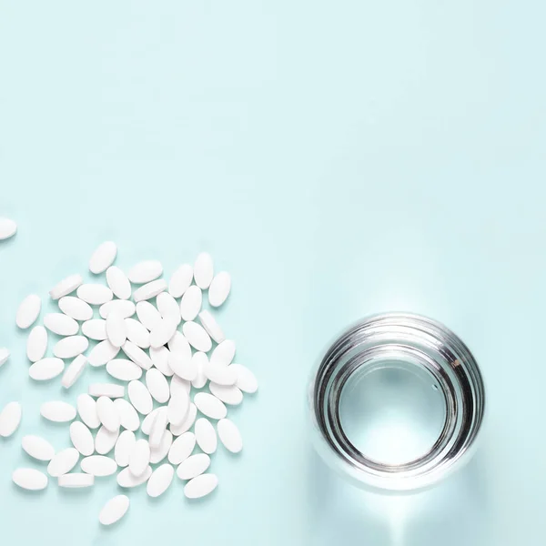 White pills with glass of clear water over blue background. Copy space composition
