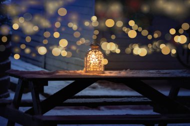 Ağaçlık bir Noel ormanlık kar manzarası. Geceleri ahşap bir masada sıcak, parlayan bir lamba..