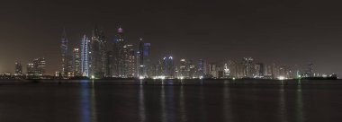 Geceleri Dubai Marina 'nın gökdelenleri. Modern binaların ışıkları, binaların önündeki Basra Körfezi denizine yansır.