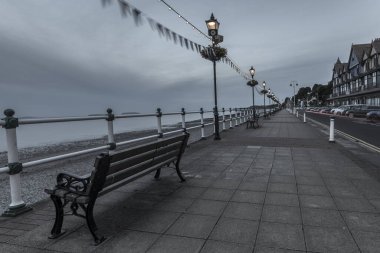 Sahile ve denize bakan bankları olan ve lamba direkleri arasında süzülen bir İngiliz rıhtımının sessiz görüntüsü..
