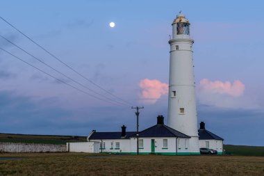 Gece gökyüzüne karşı kurulu uzun bir deniz feneri. Mavi renkli gökyüzünde ay açıkça görülüyor.