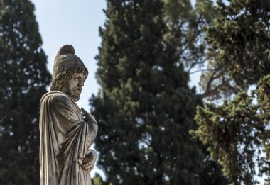 Yazları gökyüzüne ve ağaçlara karşı dikilen antik bir Roma heykeli.