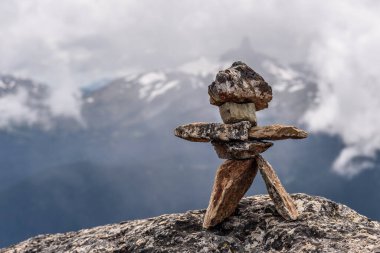 Bir Inukshuk figürü, bir dağın tepesinde duruyor, Whistler, Kanada 'da, bir dağ manzarasına bakıyor. Inukshuk, Whistler Kış Olimpiyatları 'nda sembol oldu..