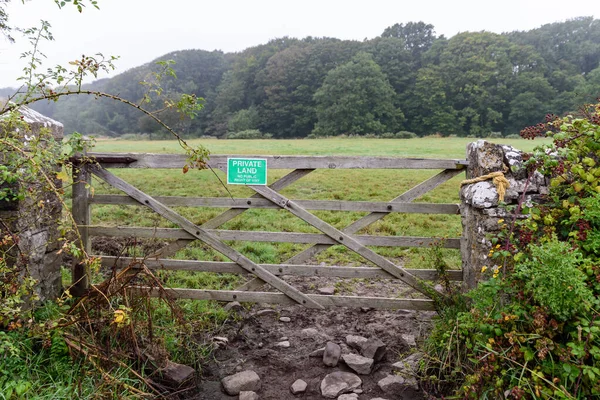 Wooden gate, leading to a rural field. The gate has a sign stating, \'Private Land\'.
