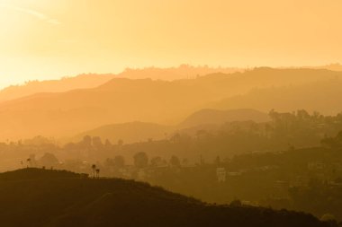 Hollywood Tepeleri üzerinde gün batımı, Los Angeles. Gökyüzü turuncu ve sarının çeşitli tonlarıdır..