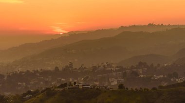 Hollywood Tepeleri üzerinde gün batımı, Los Angeles. Gökyüzü turuncu ve sarının çeşitli tonlarıdır..