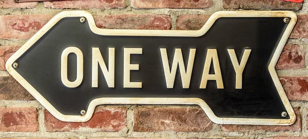 Metal one way sign, hanging on a brick wall