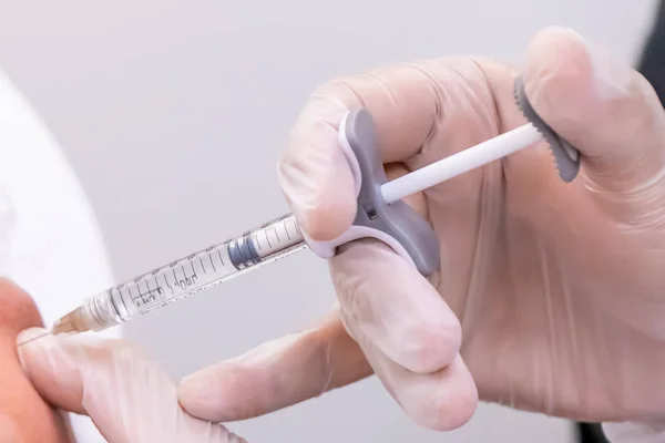 Eldivenli doktor eli, cerrahi olmayan yanak ve yüz gerdirme ameliyatı için hastaya bir şişe hyaluronik asit enjekte ediyor..