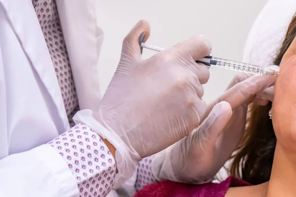 Eldivenli doktor eli, cerrahi olmayan yanak ve yüz gerdirme ameliyatı için hastaya bir şişe hyaluronik asit enjekte ediyor..