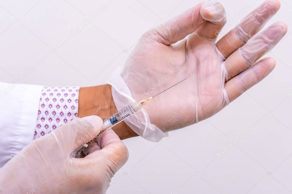 Gloved doctor hands holding an injection vial of a hyaluronic acid (HA) based dermal filler for anti-aging and volumizing face treatments.