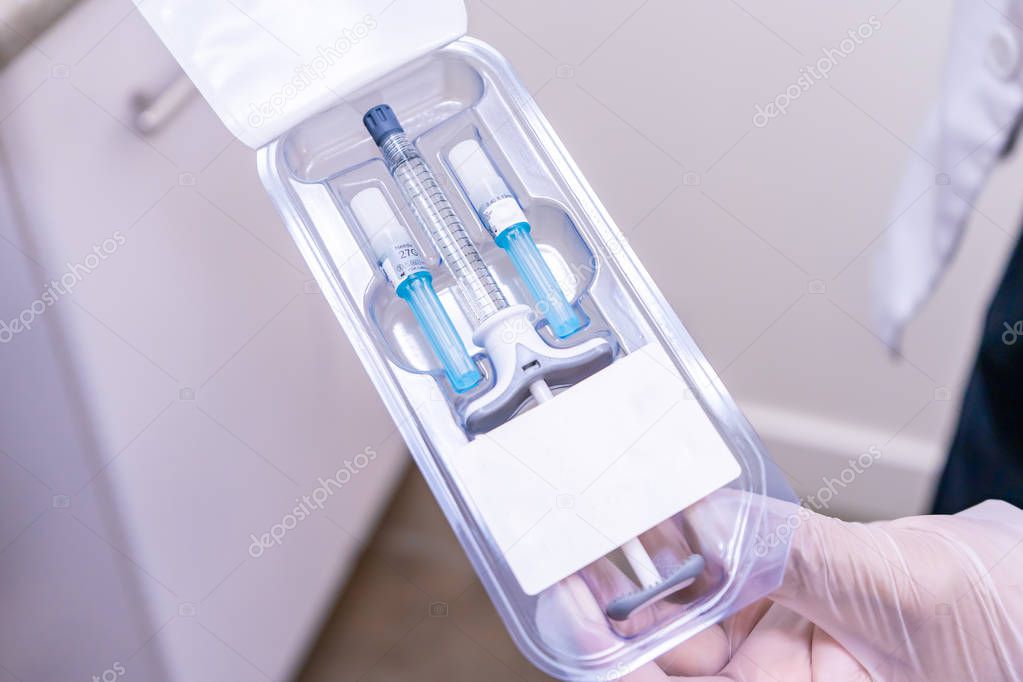 Doctor holding package of dermal filler with syringe vial and needles, for a softlift, non-surgical facelift with MD Codes on a medical cosmetic patient. Uses hyaluronic acid (HA) for anti-aging.