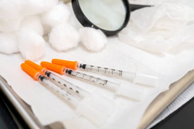 Portakal kapaklı genel iğne şırıngalarını kapatın, diyabet insülin enjeksiyonları için, ya da doktor muayenehanesinde tıbbi enjeksiyon formülleri için. Gazlı bezle tıbbi tepside büyüteçle..