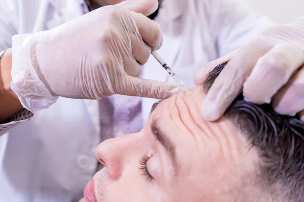 Caucasian man undergoing beauty spa botulinum neurotoxin Botox treatment for anti-aging, to smooth wrinkles as a cometic solution. Injecting forehead to relax muscles with a non-invasive procedure. — Stock Photo, Image