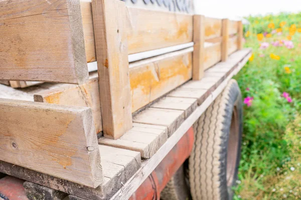 Old wooden truck trailer bed with handmade fencing and dirty tire wheel showing in a flower field — Stock Photo, Image