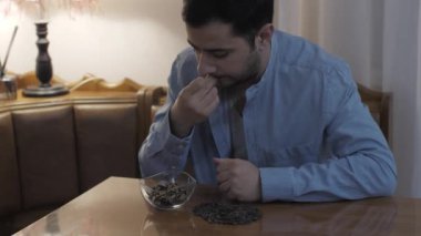 Mutfaktaki genç beyaz adam kendini izole etme karantinası sırasında ayçekirdeği yiyor.