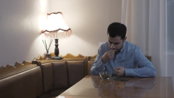 キッチンの若い白人男性は隔離中にひまわりの種を食べる — ストック動画