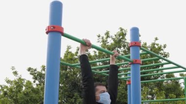 Çocuk parkında genç maskeli bir adam spor için içeri giriyor. Yükseliyor