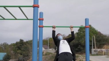 Çocuk parkında genç maskeli bir adam spor için içeri giriyor. Yükseliyor