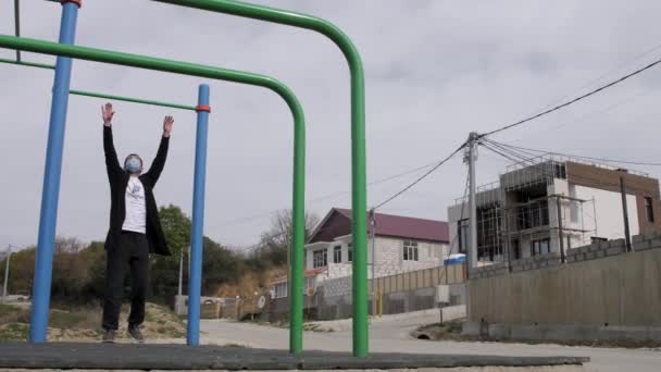 Un jeune masqué dans la cour de récréation fait du sport. se redresse — Video