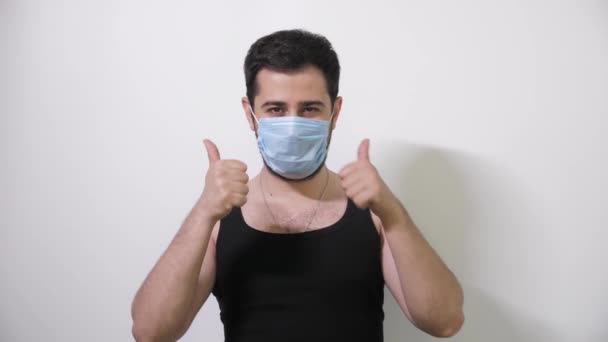 Caucasian man in medical mask shows 2 thumbs looks into camera smiles Covid19 Coronavirus — Stock Video