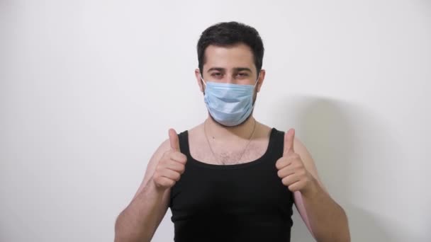 Uomo caucasico mette sulla sua maschera medica guarda nella fotocamera e due pollici verso l'alto Covid19 Coronavirus — Video Stock