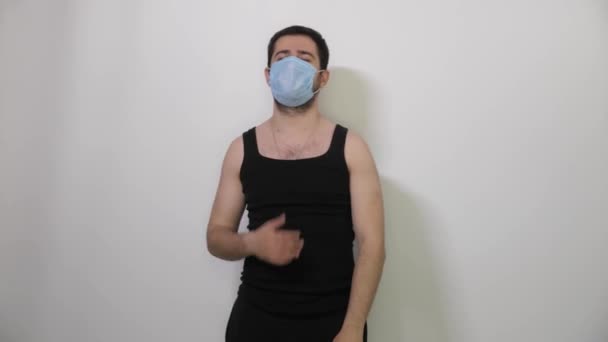 Jovem caucasiano Homem preto t-shirt usa uma máscara médica para proteger ou espalhar vírus Ri olha para a câmera — Vídeo de Stock