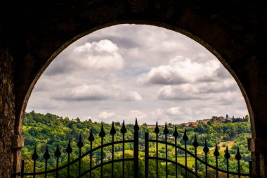 İtalya 'nın Vicenza kentindeki çayırları ve bahar ağaçları olan yeşil tepelerin manzarası yarı açık demir bir kapıdan görülüyor.