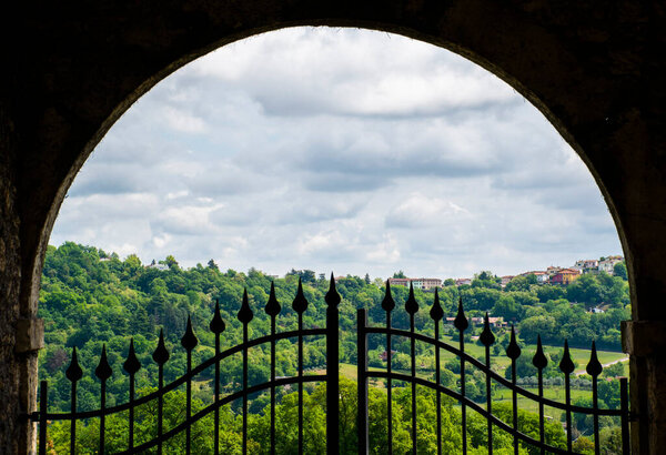panorama of green hills with pastures and spring trees in Vicenza, Italy seen from a half-open iron gate
