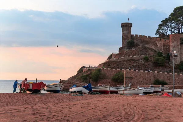 Tossa de Mar, İspanya, Ağustos 2018. Tekneler gün batımında eski bir kalenin duvarlarının yanında kıyıya çekildi..