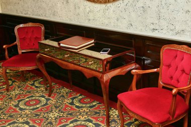 Kırmızı sandalye. Tahta bacaklı cam aynalı masa. Halı. Restoranın girişi. Koridor. Kitap cep telefonu masanın üstünde..