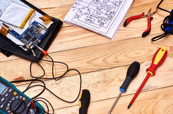 Parçalanmış tablet. Modern bozuk elektronik cihazların tamiri. Tamir aletleri. Dijital multimetre. Masaüstü elektronik aletleri. Elektronik bir cihazın şematik diyagramı.