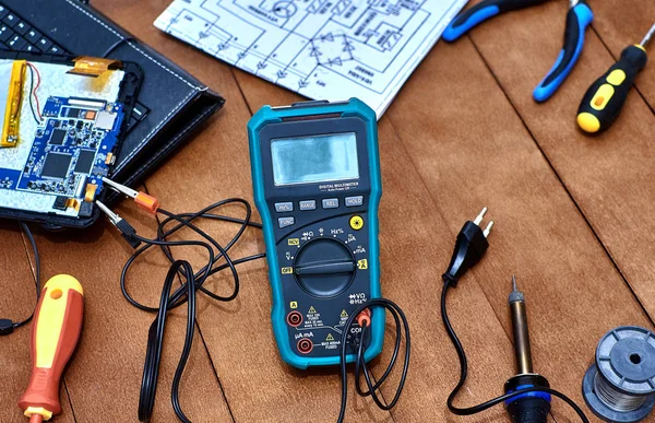 Parçalanmış tablet. Modern bozuk elektronik cihazların tamiri. Tamir aletleri. Dijital multimetre. Masaüstü elektronik aletleri. Elektronik bir cihazın şematik diyagramı.