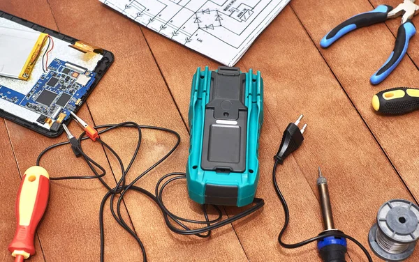 Parçalanmış tablet. Modern bozuk elektronik cihazların tamiri. Tamir aletleri. Dijital multimetre. Masaüstü elektronik aletleri. Elektronik bir cihazın şematik diyagramı.
