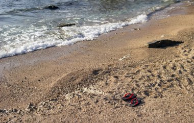 Kumda kırmızı ve siyah terlikler. Sıcak kumun yaz arkaplanı deniz veya okyanus kabarcıkları ile fotokopi alanı ile şafak veya gün batımında kart veya reklam için 