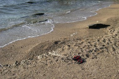 Kumda kırmızı ve siyah terlikler. Sıcak kumun yaz arkaplanı deniz veya okyanus kabarcıkları ile fotokopi alanı ile şafak veya gün batımında kart veya reklam için 
