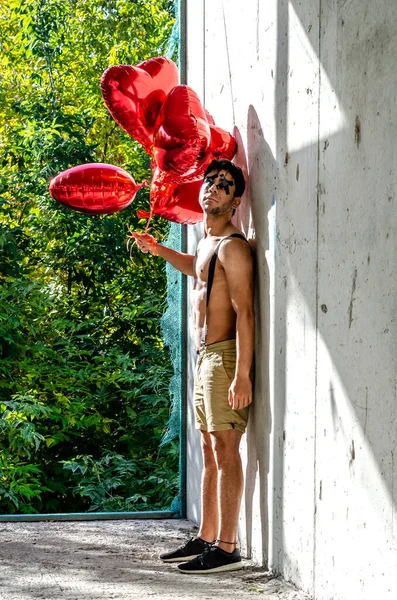O homem do Dia dos Namorados com balões em forma de coração. Jovem fica na parede de concreto — Fotografia de Stock