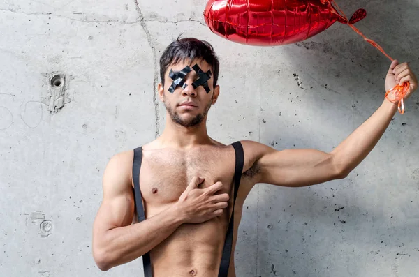 Valentine's day guy with hearts-shaped balloons. Young guy stands at the concrete wall