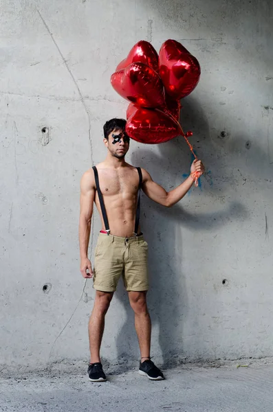 Valentine's day guy with hearts-shaped balloons. Young guy stands at the concrete wall