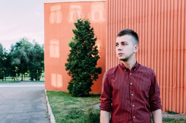 Binaların arka planında kırmızı tart gömlekli dalgın bir gencin portresi..