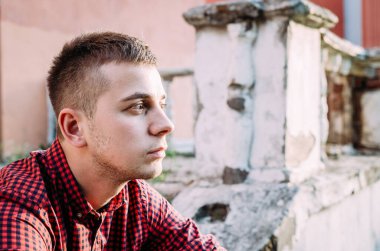 Binaların arka planında kırmızı tart gömlekli dalgın bir gencin portresi.