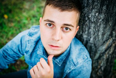 Doğada mavi kot gömlekli dalgın bir gencin portresi..